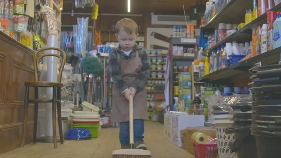 young boy wearing apron and sweeping the floor of a hardware shop for hafod hardware christmas advert